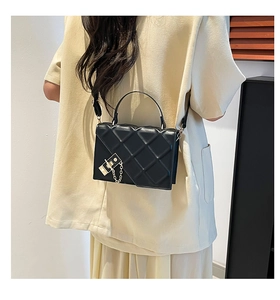 Close-up of black quilted leather shoulder bag with golden chain detail on a model