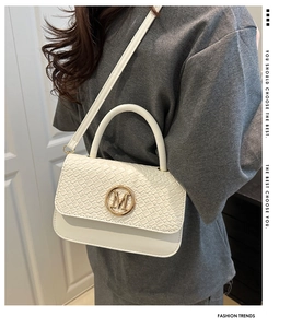 Gros plan sur un sac blanc texturé avec boucle en métal doré et lettrage M élégant