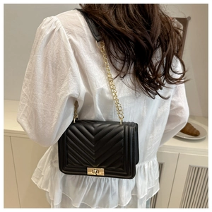 Detail of black quilted shoulder bag with V-shaped stitching and golden chain strap