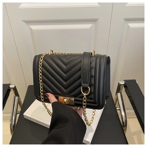 Detail of black quilted leather crossbody bag with V-shaped stitching and gold chain strap