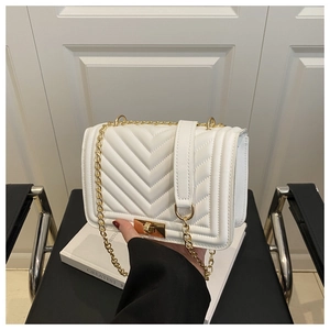 Detail view of white chevron quilted handbag with gold chain strap on a black leather chair