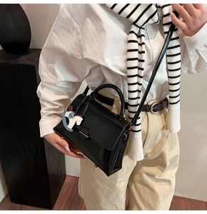 Détail d'un sac à rabat noir brillant avec breloque cheval bleu et bandoulière fine