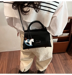Détail du sac cabas en cuir noir avec breloque cheval à bascule dans un décor chaleureux