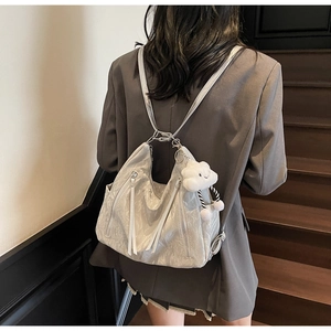 Close-up of silver wrinkled texture backpack featuring long zippers and cloud plush charm