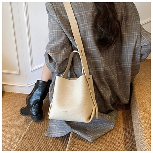 Gros plan du sac seau blanc crème en cuir porté par un mannequin en costume gris