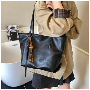 Detail of black faux leather tote bag featuring subtle texture and wooden bead tassel