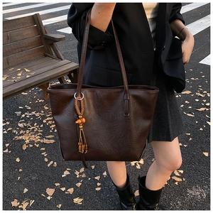 Detail of dark brown tote bag with vintage texture and woven tassel pendant on street