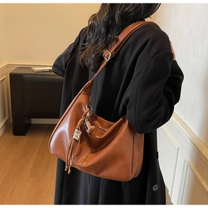Bolso hobo de cuero suave marrón con borla al hombro sobre un abrigo negro