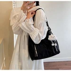 A detailed view of a black nylon shoulder bag for women with a cloud plush charm