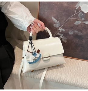 Gros plan du sac en cuir blanc avec boucle en métal et breloque cheval bleue