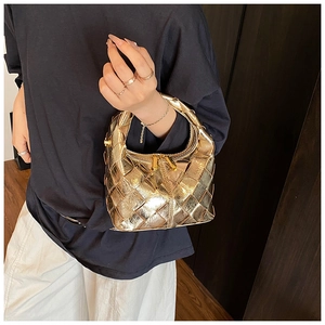 Détail de la main tenant le sac à main tressé doré avec une finition métallique chic