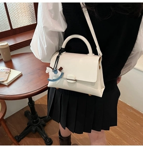 Grand sac fourre-tout blanc avec breloque cheval, exposé dans un décor de café chaleureux
