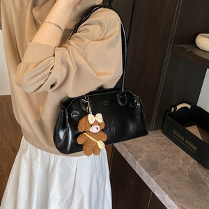 Vintage black gloss leather shoulder bag with plush bear charm in a modern home setting
