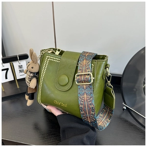 Detail of green bucket bag with gold rivets, jacquard strap, and plush rabbit charm