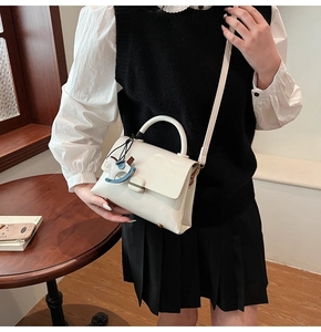 Détail d'un sac à main en cuir blanc avec boucle en métal et breloque cheval en intérieur