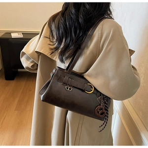 Detail of dark brown leather shoulder bag featuring a unique pretzel charm and gold hardware