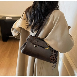 Detail of dark brown retro pillow bag with metal buckles and pendant on a trench coat