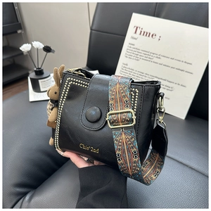 Detail of black leather bucket bag featuring gold studs and ethnic print wide strap