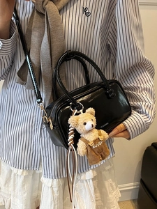 Chic black patent leather boston bag with bear pendant on striped shirt background