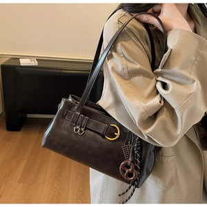 Detail of dark brown leather shoulder bag with gold buckle and pretzel charm accent