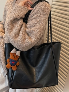 Minimalist black leather tote bag with thin straps and a cute brown bear charm