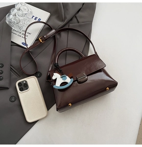 Détail d'un sac à main en cuir marron foncé avec fermoir carré et breloque cheval coloré