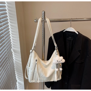 Detail of off-white tote bag featuring dual front zippers and a plush cloud charm accessory