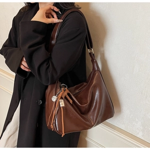 Detalle de bolso hobo grande marrón oscuro con borla de cuero y colgante metálico