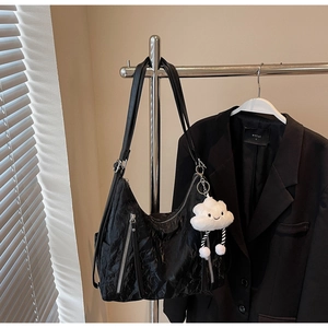 Detail of black pleated shoulder bag with metallic zippers and white cloud plush charm
