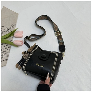 Detail view of black leather bucket bag with gold studs and printed wide shoulder strap