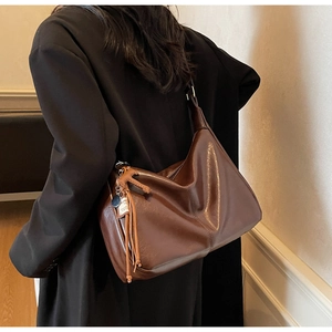Detalle de bolso hobo de cuero marrón suave con borla de flecos y colgante minimalista