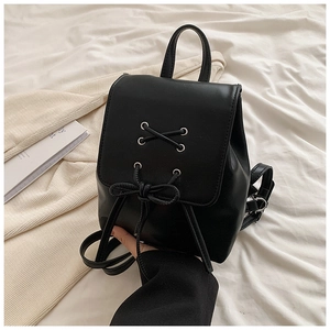 Detail eines schwarzen PU-Lederrucksacks mit Metallösen und dekorativer Schleife auf Bett