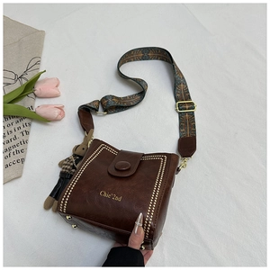 Close-up of brown bucket bag with gold rivets, rabbit charm, and patterned strap