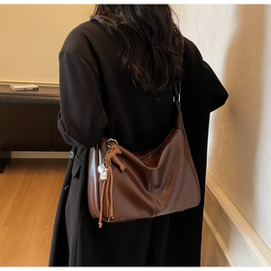 Bolso hobo marrón oscuro en modelo con abrigo negro con borlas y colgante de caballo