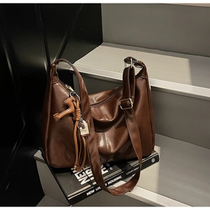 Detalle de bolso hobo marrón oscuro en cuero sintético con borla decorativa de metal
