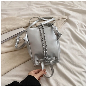 Detailansicht eines silbernen Metallic-Mini-Rucksacks mit Kettenriemen auf weißem Stoff