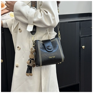 Detail of black leather bucket bag with gold studs and cute brown rabbit doll pendant