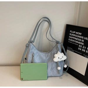 Light blue nylon crossbody bag with dual zippers and plush charm next to a tablet