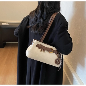 Detail of cream shoulder bag featuring brown leather straps and decorative metal rings