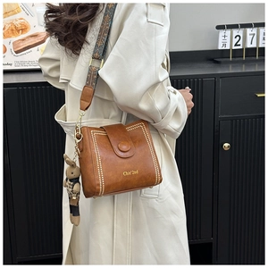 Brown leather bucket bag with rivet trim, woven strap, and cute rabbit charm detail