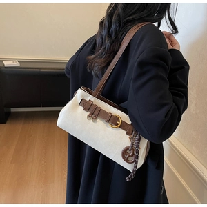 Detail view of canvas and leather shoulder bag with decorative pretzel charm and gold buckle