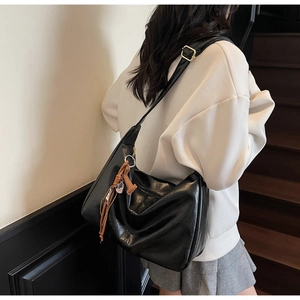 Detalle del bolso hobo negro brillante con borla de cuero marrón en modelo con sudadera