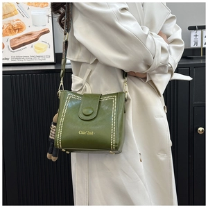 Detail of dark green bucket bag with gold rivets, jacquard strap and bear pendant
