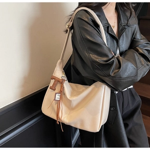Detalle de un bolso hobo crema vintage con borla y amuleto de la letra T