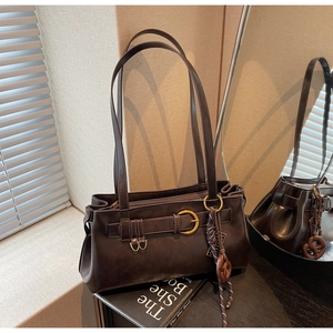 Detail of dark brown retro shoulder bag with golden buckle and woven cord pendant