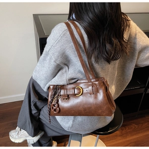 Close-up of retro brown shoulder bag with decorative metal buckle and unique knot charm