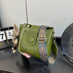 Olive green bucket bag with retro wide strap and plush charm in a vintage setting