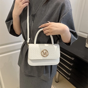 Sac à main blanc tressé avec logo M doré porté par un mannequin dans un style épuré