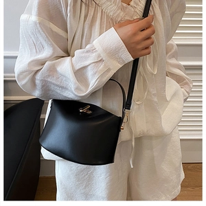 Detail of minimalist black leather handbag with elegant gold twist lock and slim strap