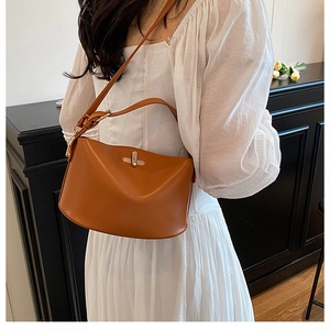 Braune Leder-Eimertasche mit Metallschloss an Model im weißen Kleid präsentiert
